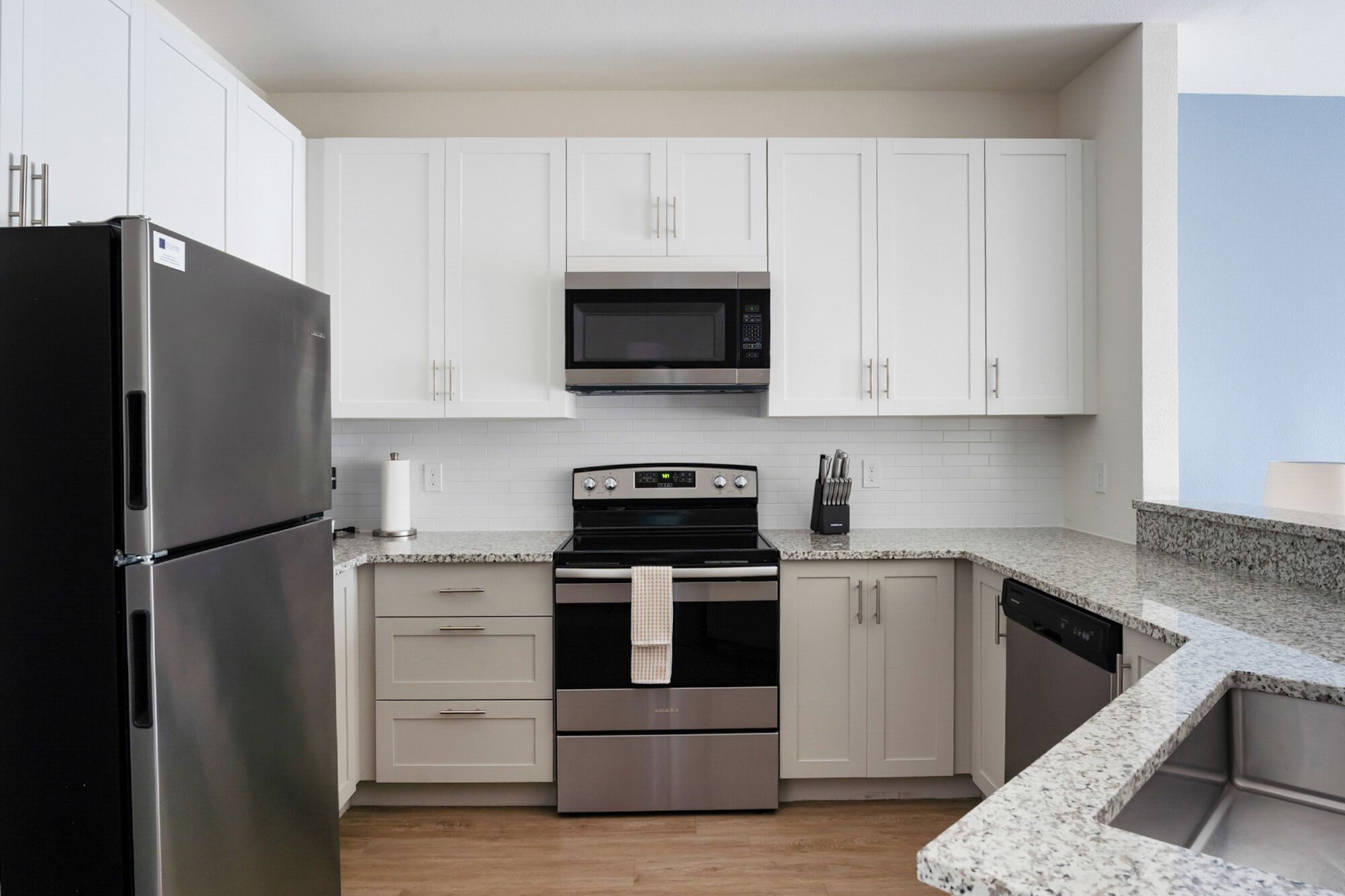 A modern kitchen with white cabinets, a stainless steel refrigerator, a microwave, an oven, and a dishwasher.