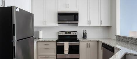 A modern kitchen with white cabinets, a stainless steel refrigerator, a microwave, an oven, and a dishwasher.