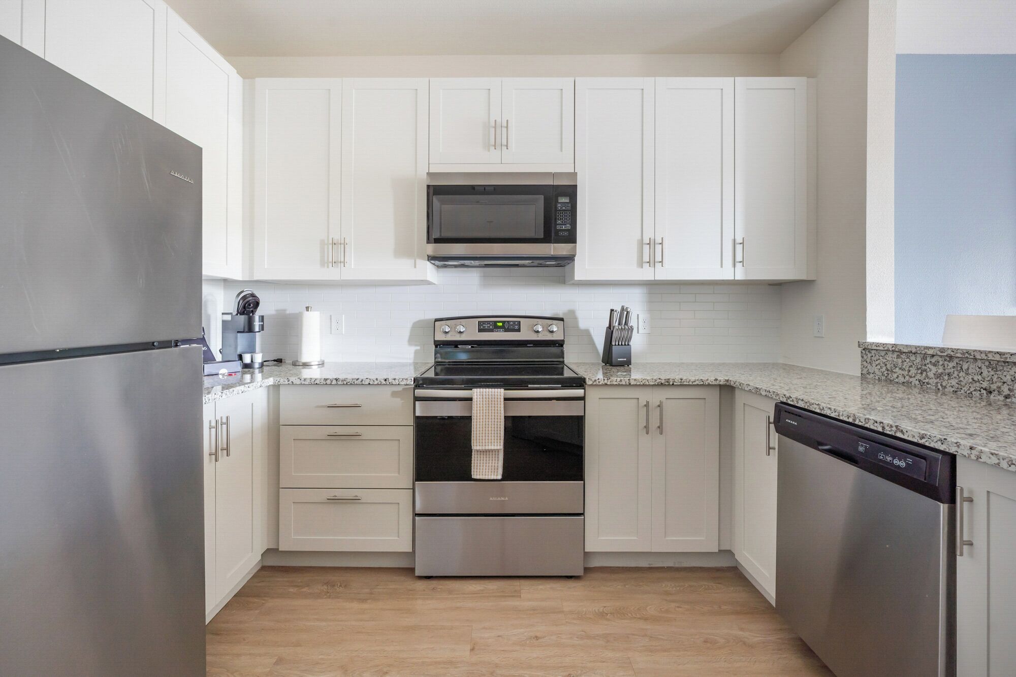 A compact kitchen with white cabinets, a stainless steel refrigerator, a microwave, an oven, and a dishwasher.