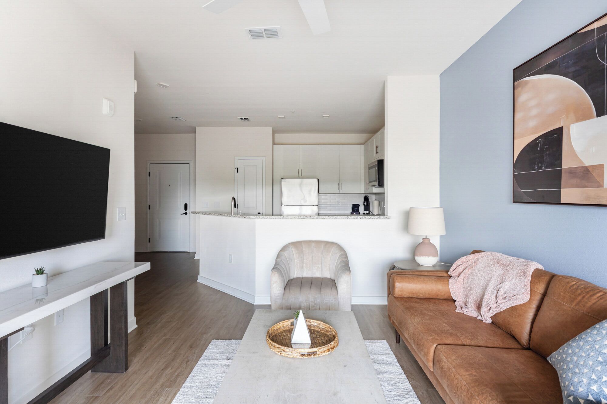 Een moderne woonkamer met een flatscreen televisie, een bruine leren bank, een salontafel en een keuken op de achtergrond.