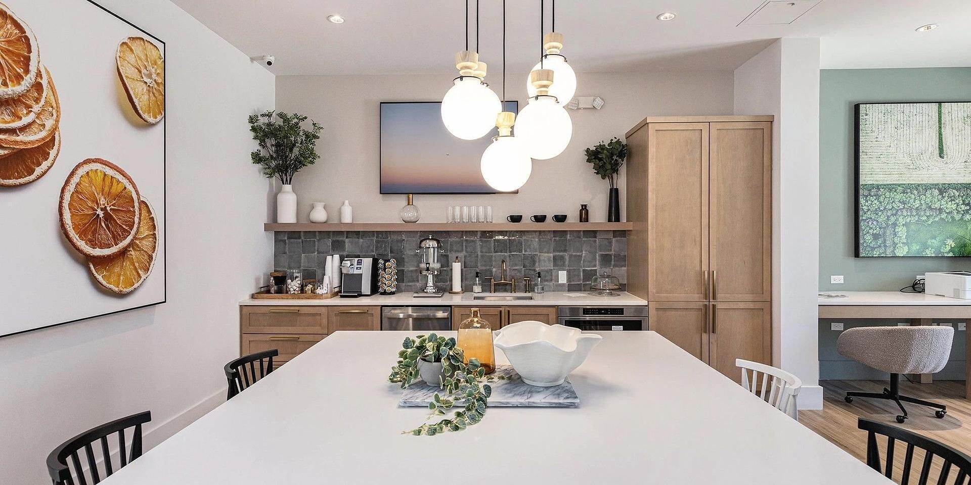 A modern kitchen with a central island, pendant lighting, and a large flat-screen TV.