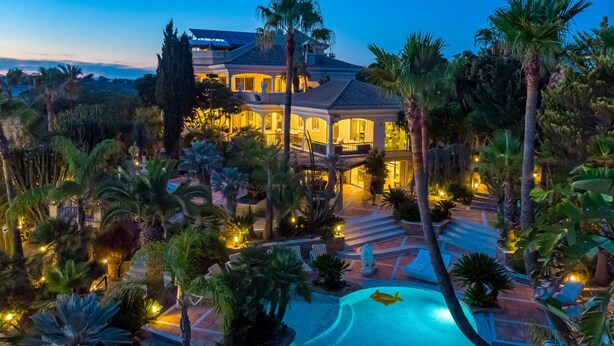 Une grande maison avec une piscine, entourée de palmiers et de plantes.