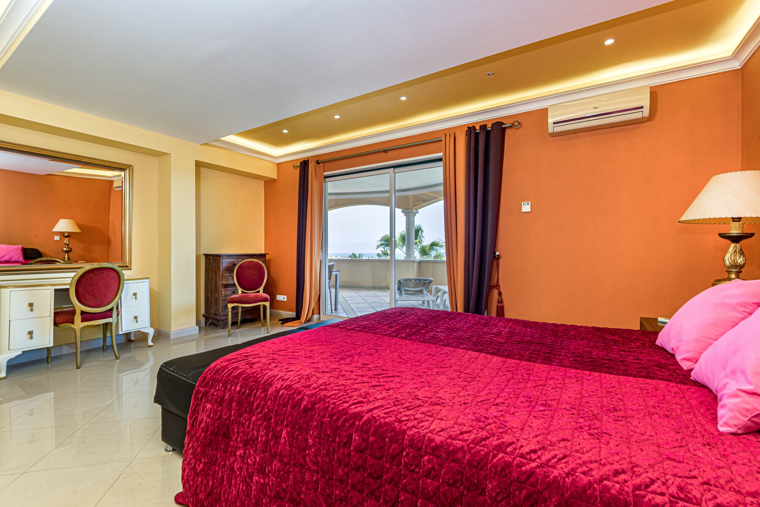 Hotelkamer met een groot bed, een bureau met stoel, een balkon met uitzicht en een airconditioning.