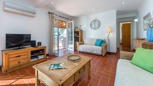 Ein Wohnzimmer mit Fernseher, Holzmöbeln, einer Couch, einem Couchtisch und einer Wanduhr.