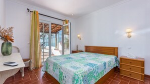 Ein Schlafzimmer mit einem Bett, einem Nachttisch, einer Holzkommode, einem Schreibtisch mit Stuhl und einem Fenster mit Vorhängen.