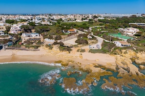 An aerial view of a coastal residential area with houses, a beach, and rocky terrain. - Villa Mimao boasts the perfect location almost directly on the wonderful beach of Manuel Lourenço (Albufeira)