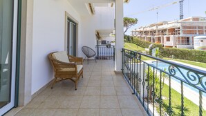 Ein Balkon mit einem Korbstuhl, einem gepolsterten Stuhl und einem kleinen Tisch. Im Hintergrund ist ein Schwimmbad und eine Baustelle zu sehen.