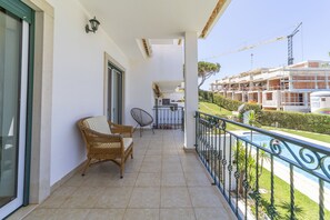 A balcony with a wicker chair, a cushioned chair, and a small table. There is a view of a swimming pool and a construction site in the background. - Villa Moises  - an excellent property 500 mts from the famous Falésia beach (Albufeira)