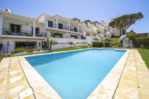A swimming pool with a geometric tile pattern, surrounded by a stone deck. There are white buildings with balconies and a tree in the background. - Villa Moises  - an excellent property 500 mts from the famous Falésia beach (Albufeira)