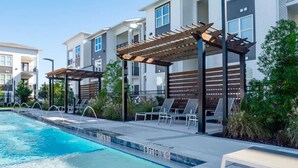 A swimming pool with a wooden pergola and lounge chairs, surrounded by apartment buildings. - Landing Apartments Near North Okaloosa Medical Center (Crestview)