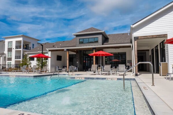 A swimming pool with lounge chairs and umbrellas, surrounded by buildings with balconies and large windows.