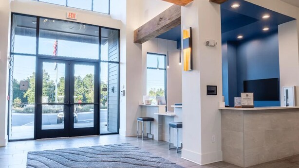 A reception area with a large glass door, a reception desk, and a blue accent wall. - Landing Apartments Near North Okaloosa Medical Center (Crestview)