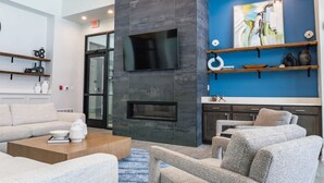 A modern lobby with a fireplace, seating area, and blue accent wall. - Landing Apartments Near North Okaloosa Medical Center (Crestview)
