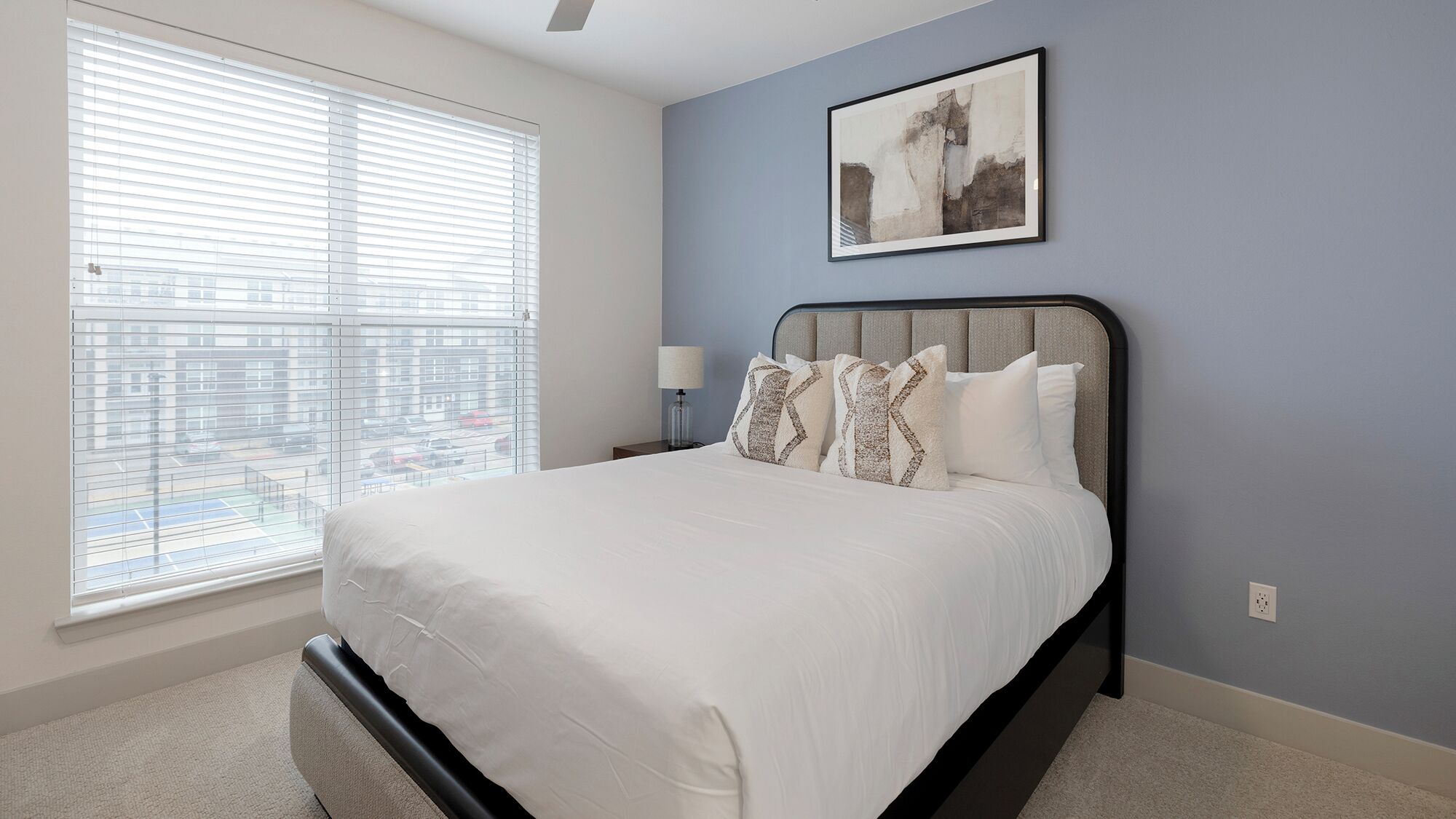 A bedroom with a bed, a nightstand, a lamp, and a window with blinds.