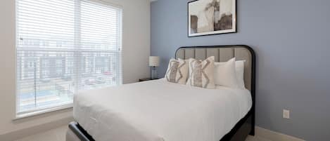 A bedroom with a bed, a nightstand, a lamp, and a window with blinds.