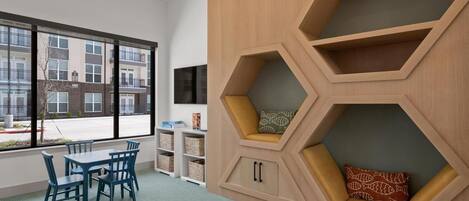 A modern room with a large window, a dining area with blue chairs, and a unique hexagonal shelving unit with cushions.