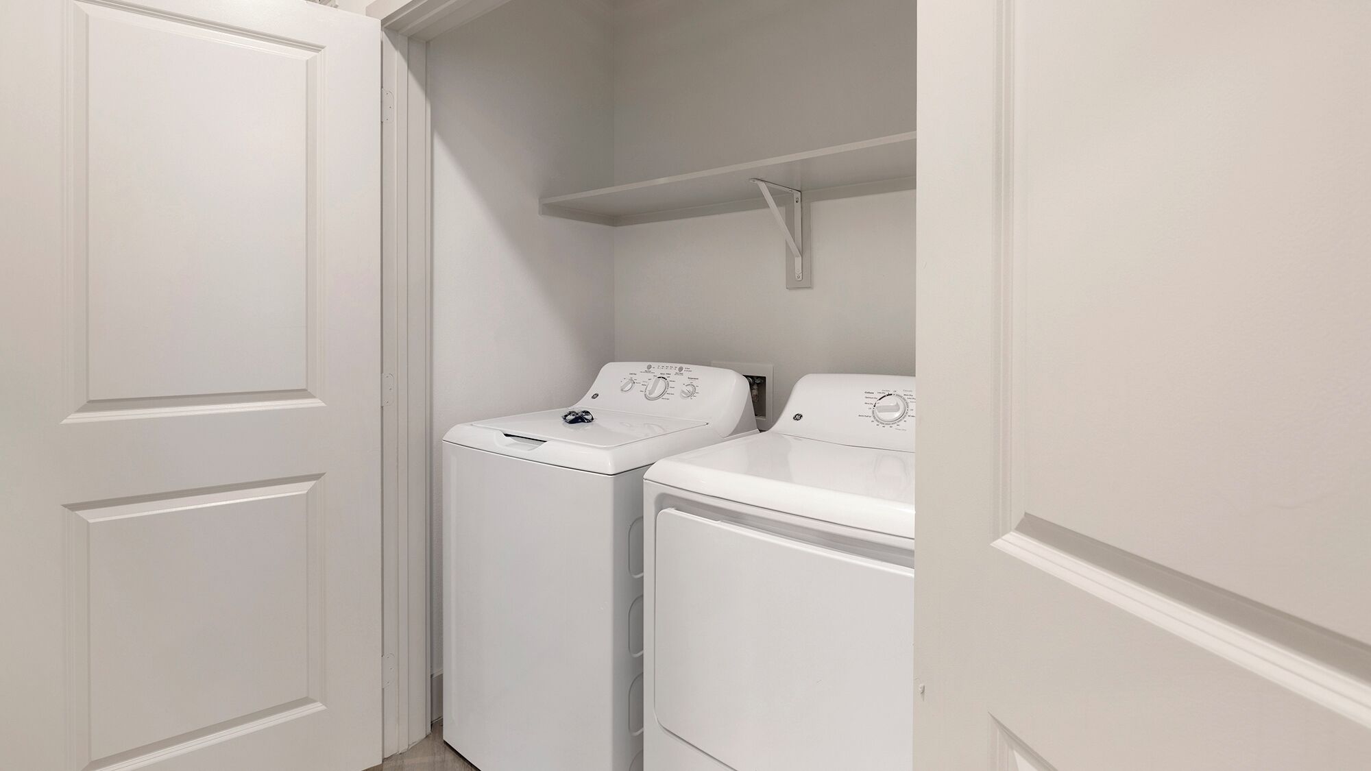 A laundry room with two white washing machines and a shelf above them.