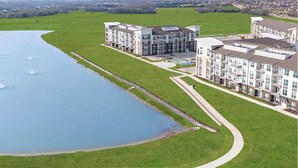 A modern apartment complex with a large body of water and a well-maintained lawn. - Landing Furnished Apartments - Garland (Sachse)