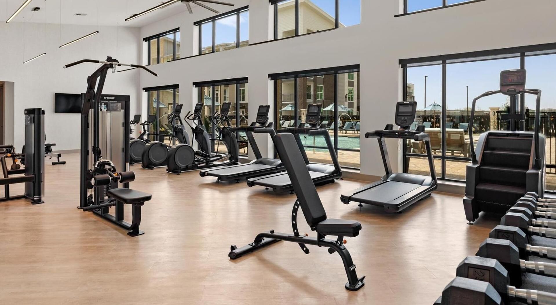 A modern gym with various exercise equipment, large windows, and a pool view.