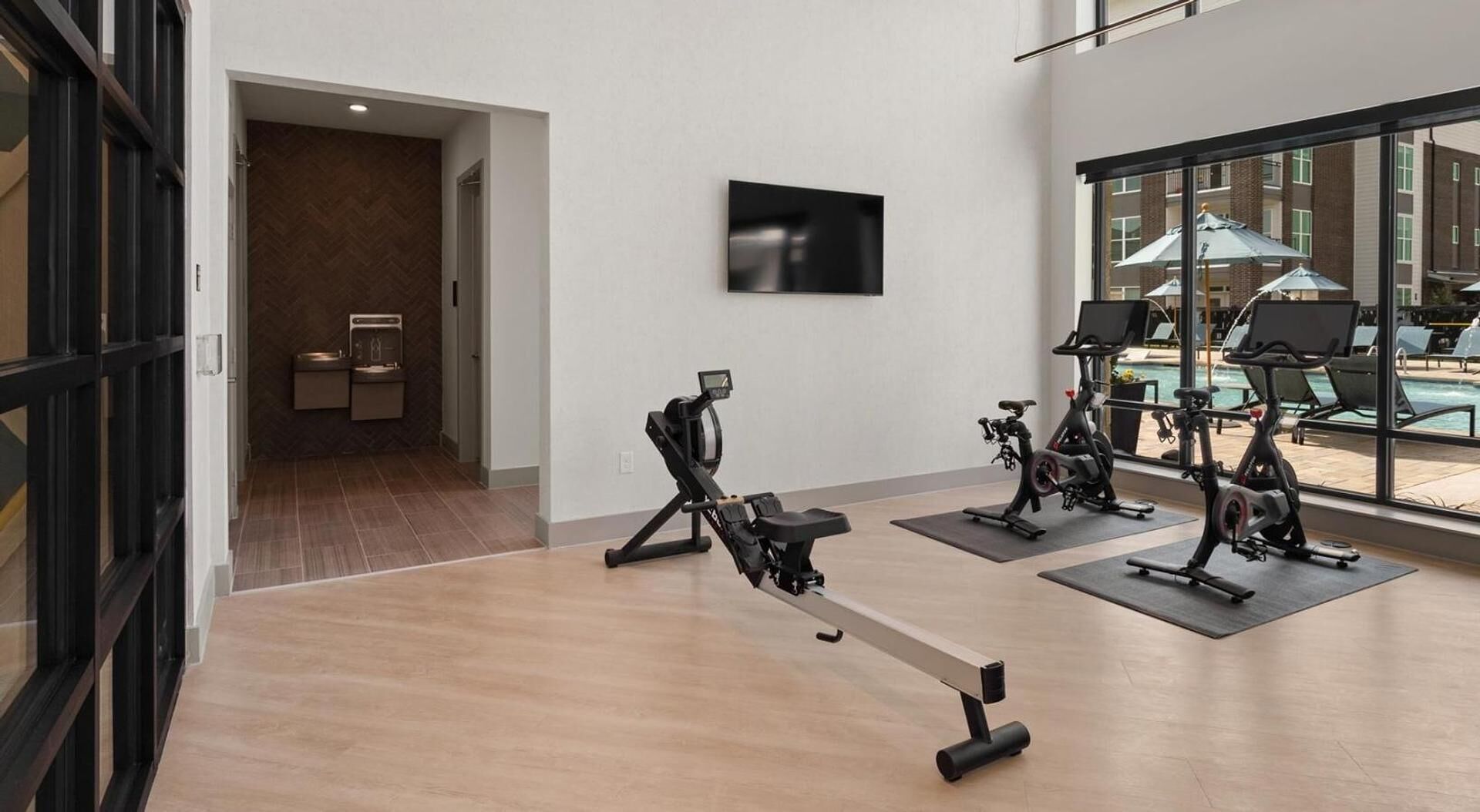 Un gimnasio con bicicletas estáticas, televisión y vista a la piscina.
