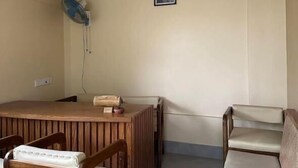 Une pièce comprenant une table en bois, deux chaises, un canapé, un ventilateur fixé au mur et un tableau encadré.