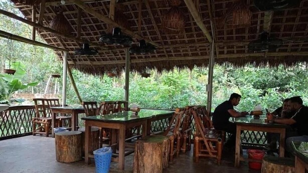 Un espace de restauration en plein air, avec des tables et des chaises en bois, entouré d’une végétation luxuriante.