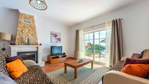 Ein Wohnzimmer mit Kamin, Fernseher und Blick ins Freie.