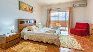 Ein Schlafzimmer mit Bett, Nachttisch, rotem Sessel und einem Bild an der Wand.