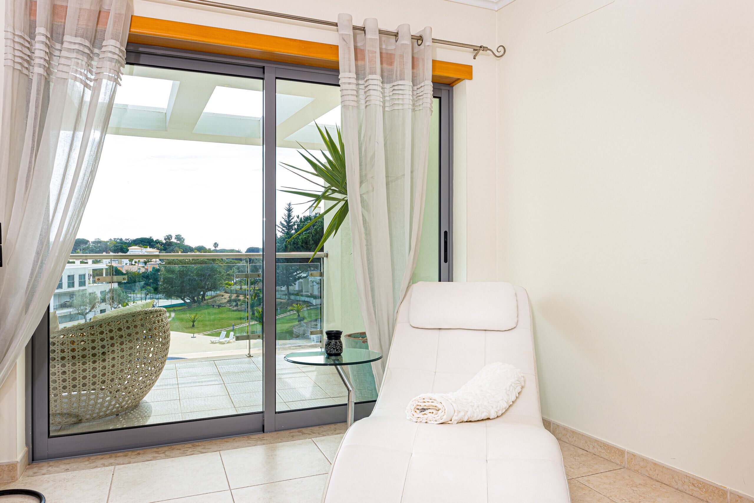 Un balcon avec une chaise blanche, une table en verre et une vue sur un jardin et des immeubles.