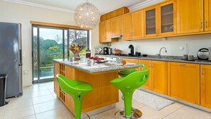 A modern kitchen with wooden cabinets, a large island with bar stools, and a view through the glass door. - Villa Seashell is a specious 3 bedroom townhouse on Monte da Balaia (Albufeira)