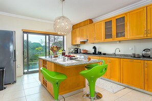 A modern kitchen with wooden cabinets, a large island with bar stools, and a view through the glass door. - Villa Seashell is a specious 3 bedroom townhouse on Monte da Balaia (Albufeira)