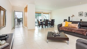 A spacious living room with a black leather sofa, a coffee table, and a dining area with a table and chairs. - Villa Seashell is a specious 3 bedroom townhouse on Monte da Balaia (Albufeira)