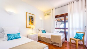 A hotel room with two beds, a window with curtains, a wooden chair, and a painting on the wall.