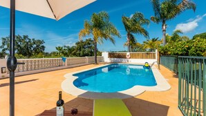 A swimming pool with a wooden deck, a bottle of wine, and a glass of wine on the deck.