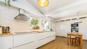 A modern kitchen with white cabinetry, a wooden countertop, and a dining area with a wooden table and bench.
