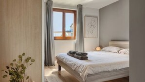 Una camera da letto con un letto grande, una finestra con tende, un comodino con una lampada e un'opera d'arte incorniciata al muro.