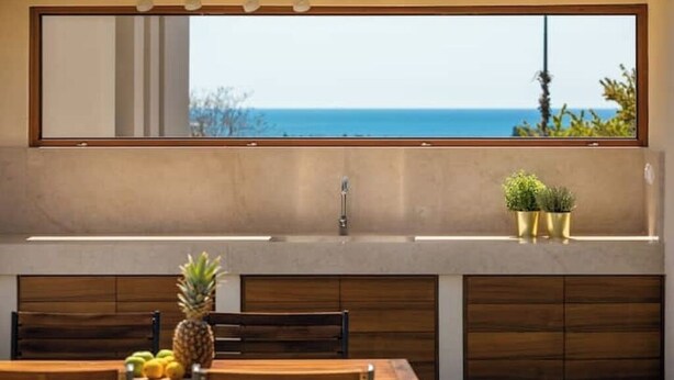 Una cucina con vista sull'oceano, un tavolo da pranzo in legno con frutta e una piccola pianta in vaso.