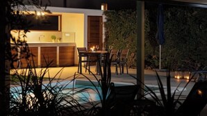 Un'area cucina esterna con tavolo e sedie, una piscina e una zona salotto coperta.