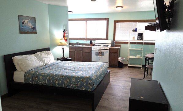 Une chambre comprenant un lit, une table de chevet, une lampe, une petite kitchenette avec une cuisinière, et un coin repas avec une table et des chaises.
