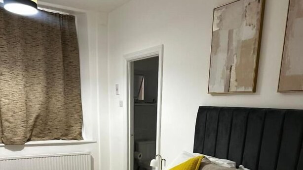 Habitación de hotel con cama, ventana con cortinas, radiador y puerta que da a un baño.