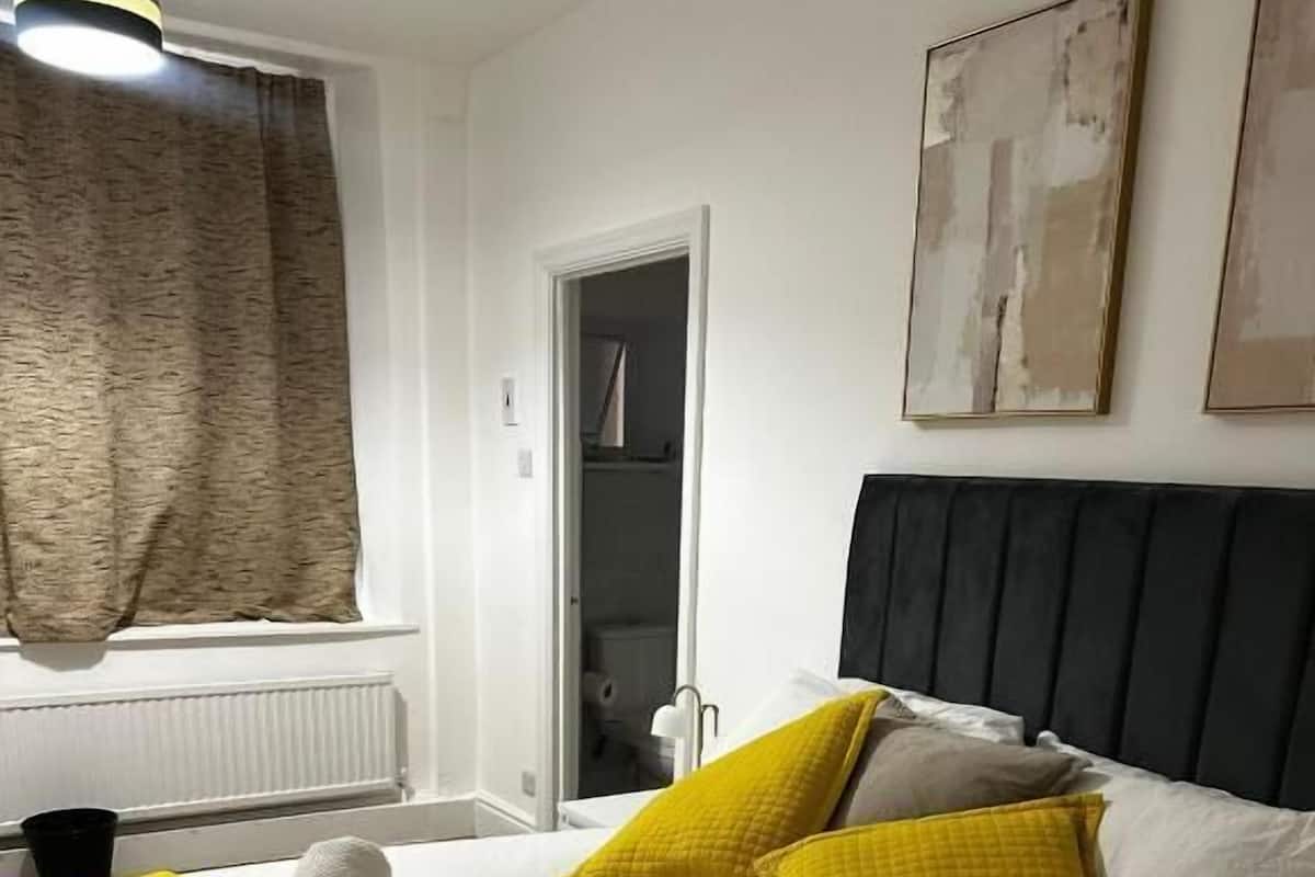Une chambre d’hôtel avec un lit, une fenêtre avec des rideaux, un radiateur et une porte donnant sur une salle de bain.