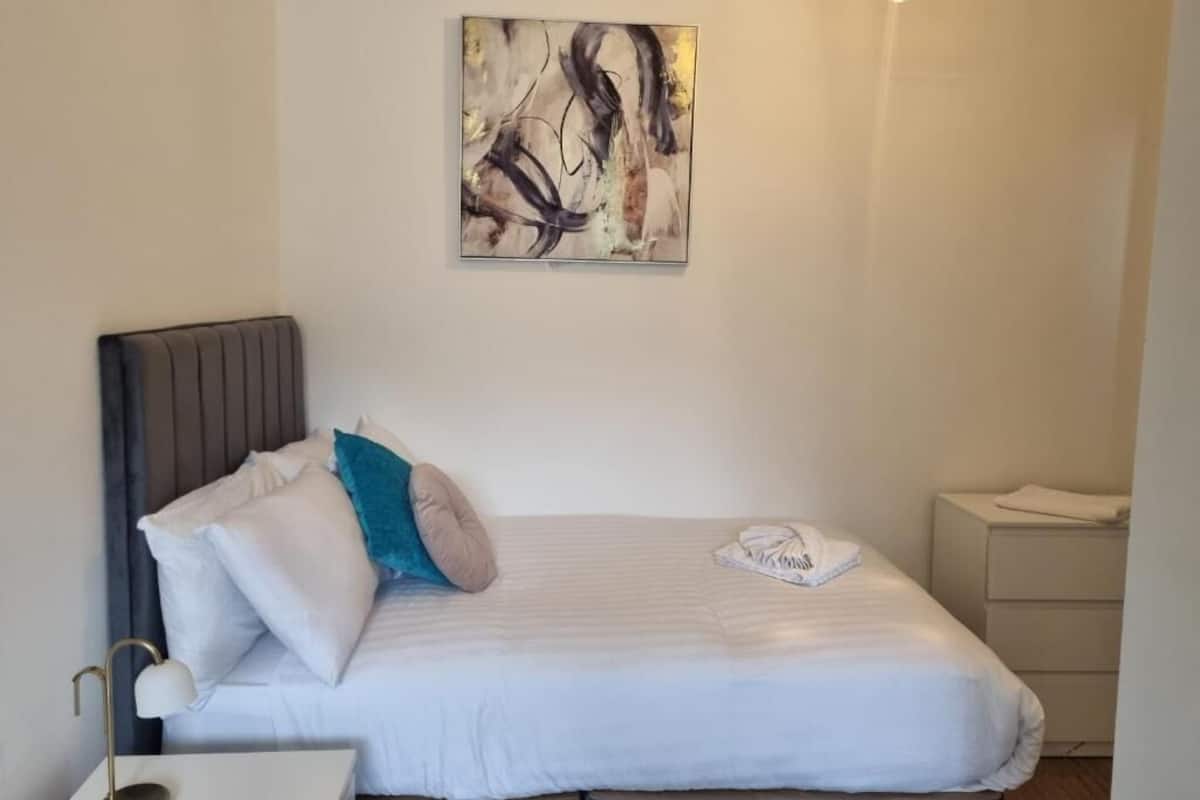 Un lit bien fait, avec une tête de lit, une lampe de chevet et une serviette pliée posée sur la table de chevet.