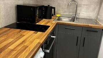 A compact kitchen with a wooden countertop, a built-in oven, a sink, and grey cabinets.