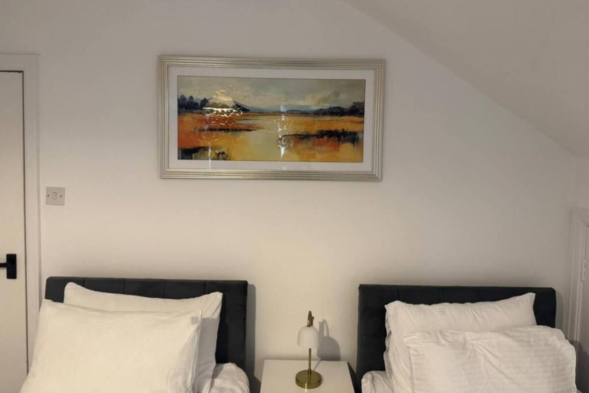 Une chambre d’hôtel avec deux lits, une table de chevet, une lampe et un tableau encadré au mur.