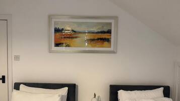 Ein Hotelzimmer mit zwei Betten, einem Nachttisch, einer Lampe und einem gerahmten Gemälde an der Wand.