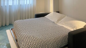 Ein Hotelzimmer mit Bett, Stuhl, Schrank und einem Fenster mit Vorhängen.