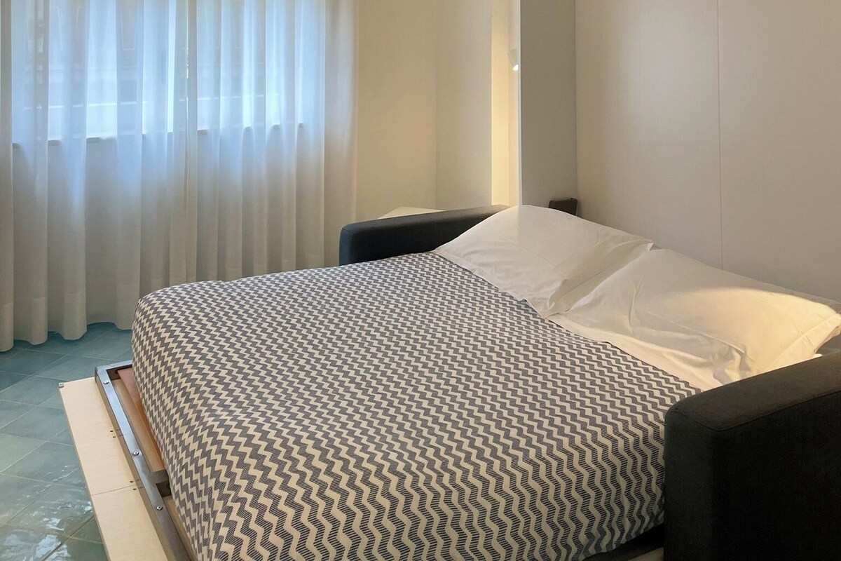Ein Hotelzimmer mit Bett, Stuhl, Schrank und einem Fenster mit Vorhängen.