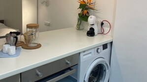Ein kleiner Waschbereich mit Waschmaschine, Kaffeemaschine, einer Pflanze und einer Pendelleuchte.