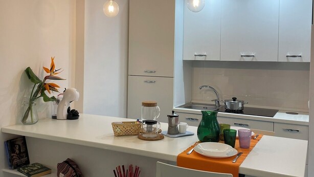 Eine moderne Küche mit weißen Schränken, einer zentralen Kochinsel mit Kaffeemaschine und Pendelleuchten.