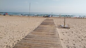 A sandy beach with a wooden walkway leading to the water, footprints, and a lifeguard stand.
